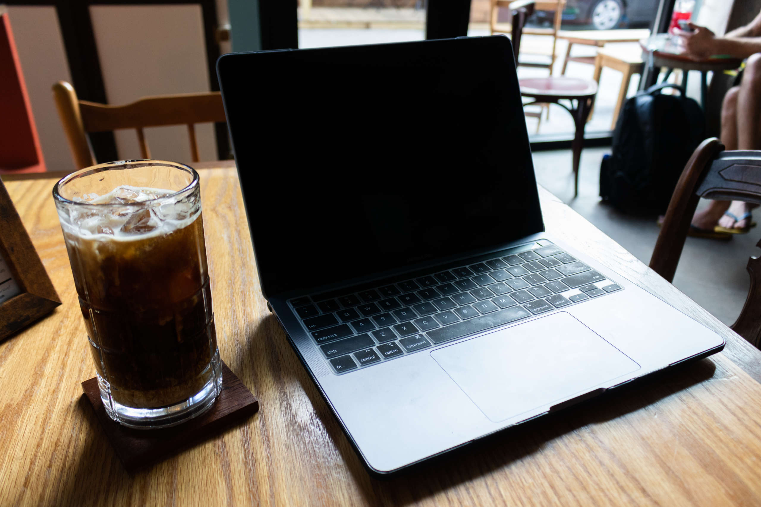 A laptop sits on a wooden table in a cafe.