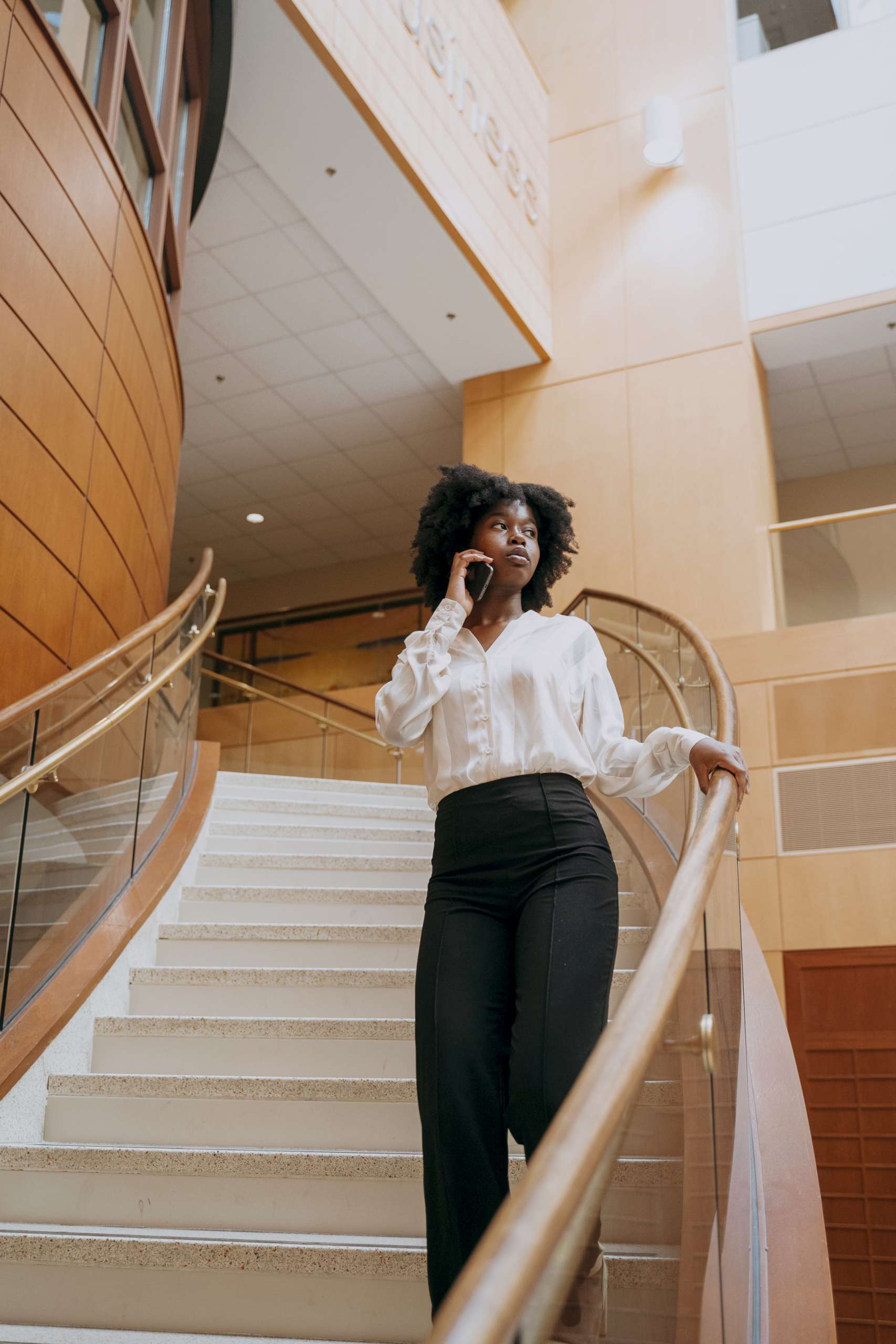 Professional black woman stands in stairwell on cellphone.