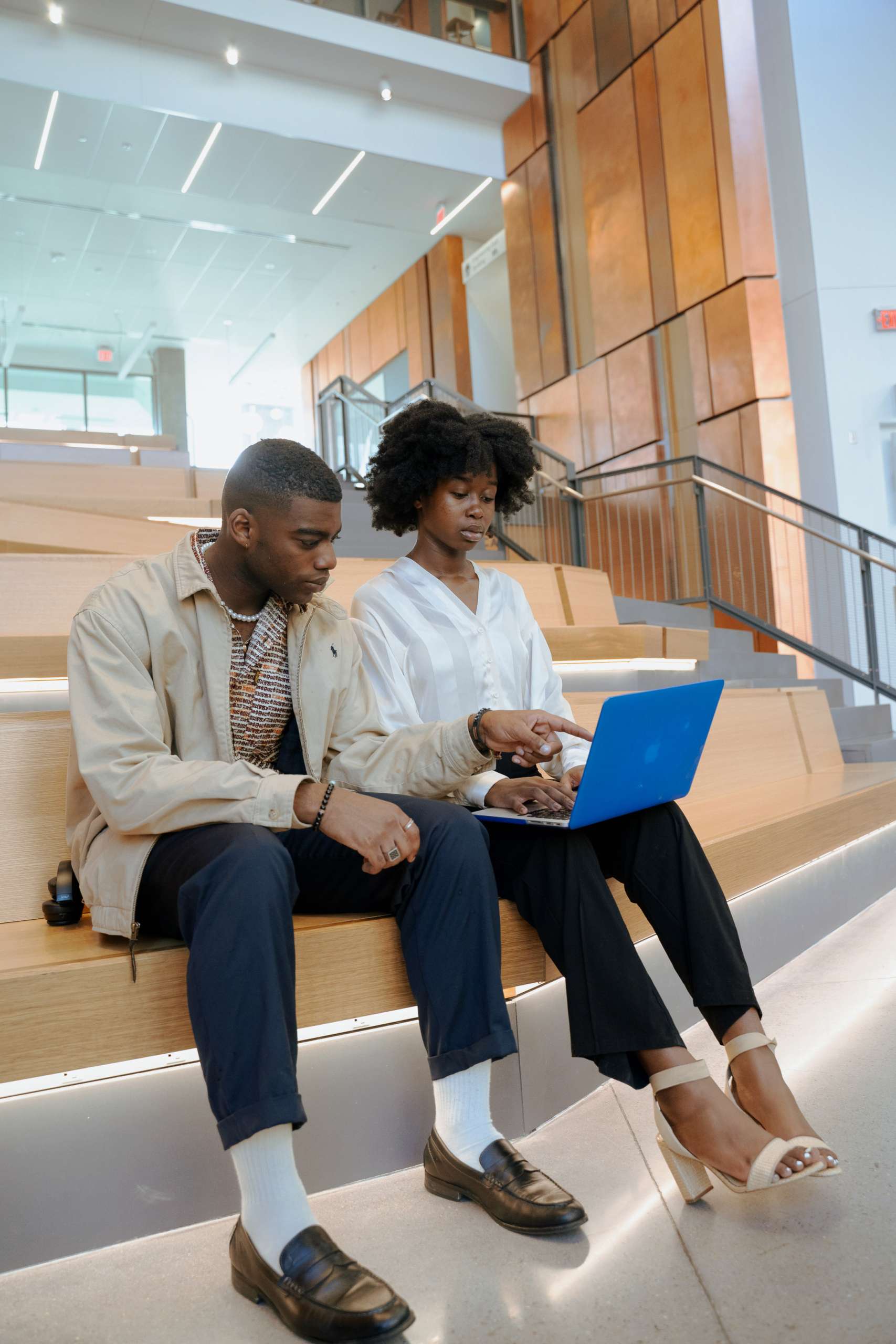 Two young black professionals sit looking at a laptop.