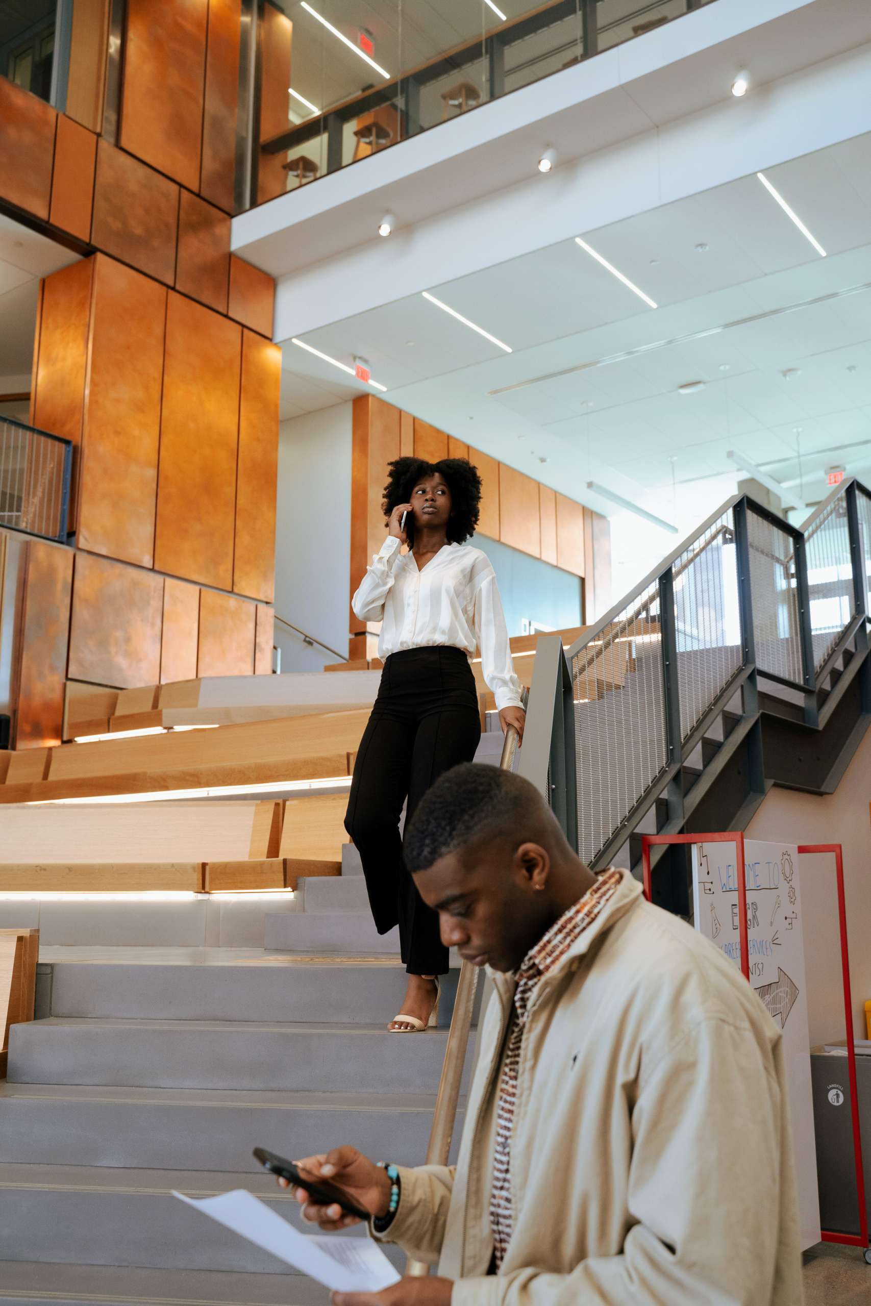 Two young black professionals stand around a staircase.