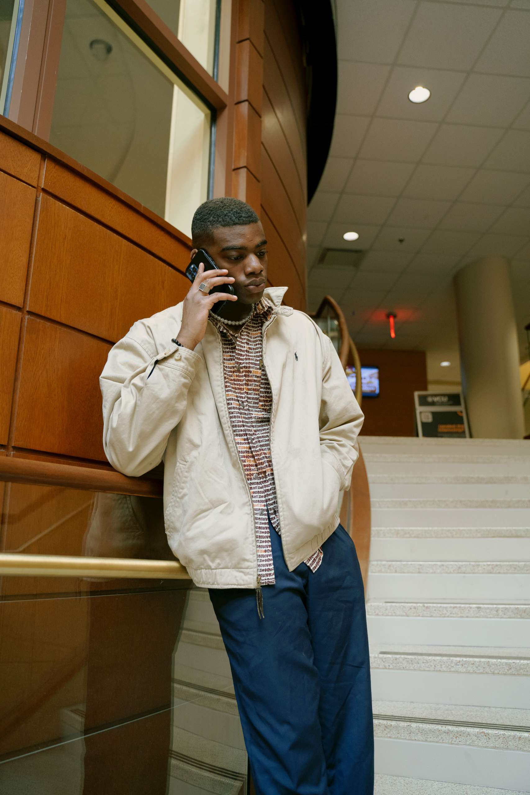 Young black man stands in stairwell on the phone.