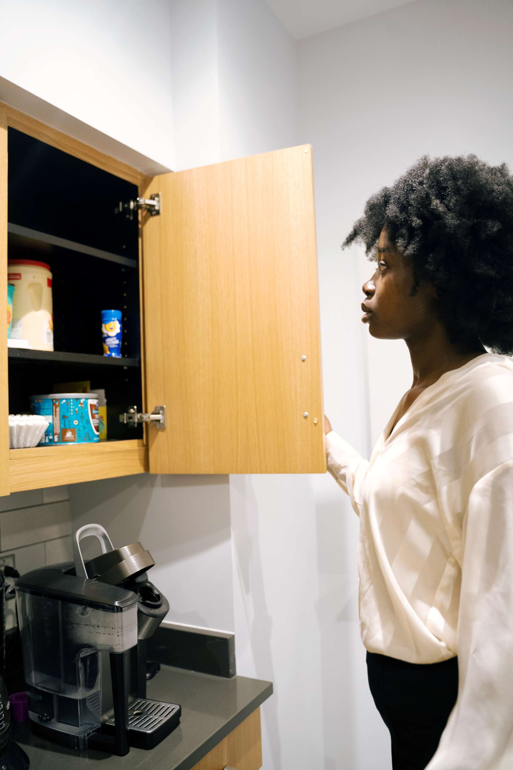 Young black woman looks at open cabinet.