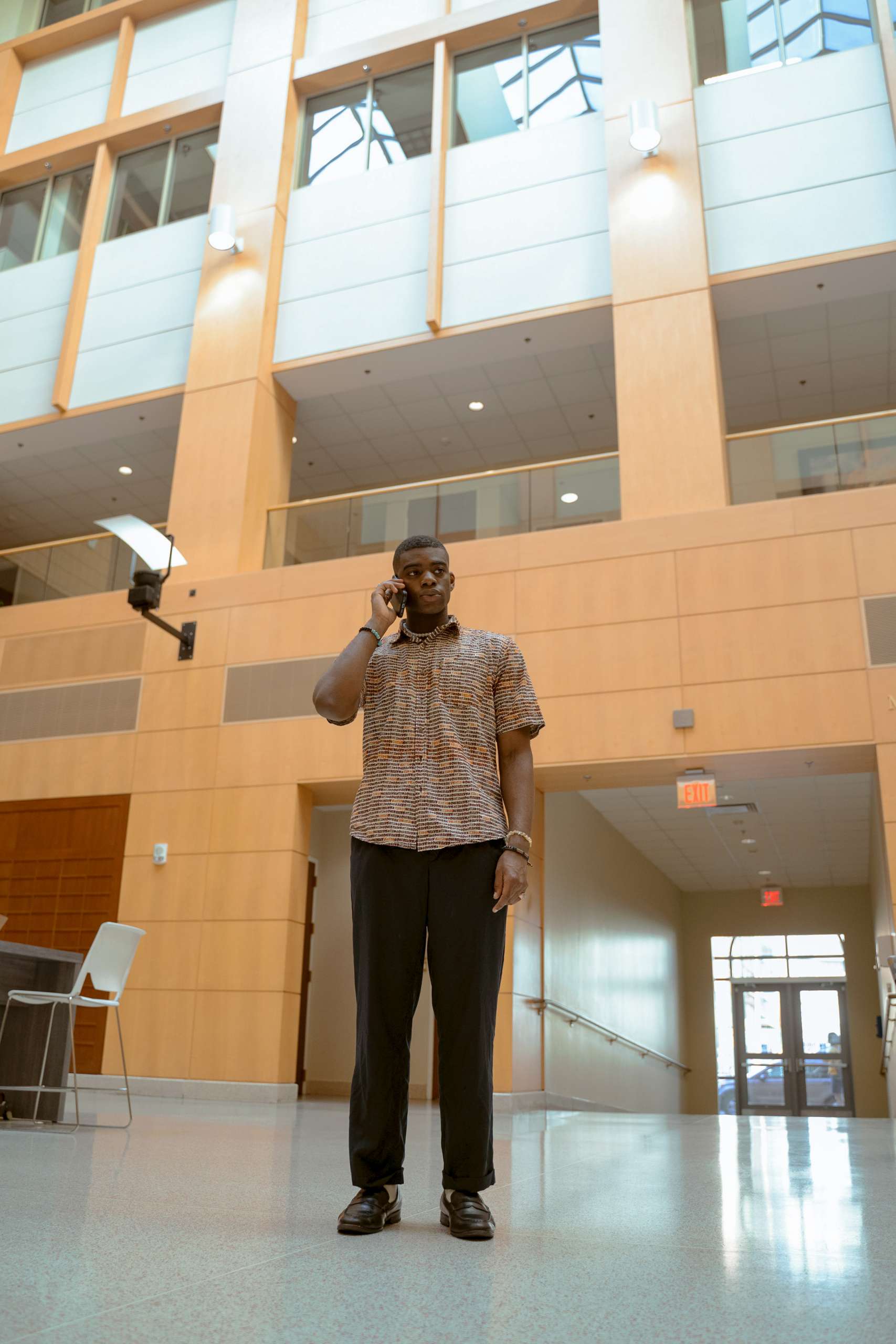 Young professional black man stands in lobby on cellphone.