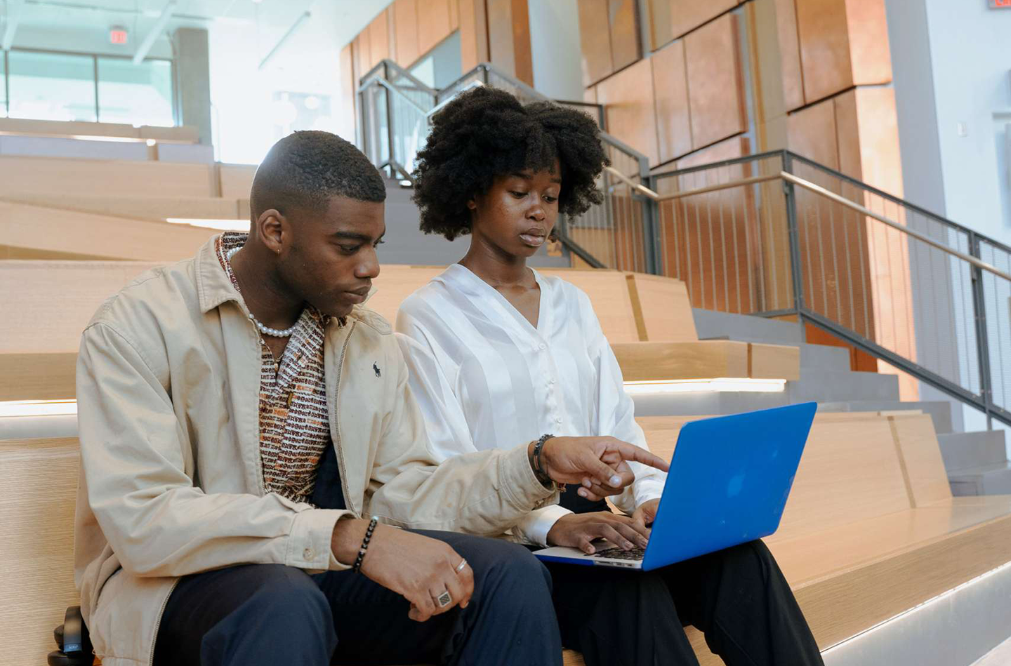 Two young black professionals sit looking at a laptop.